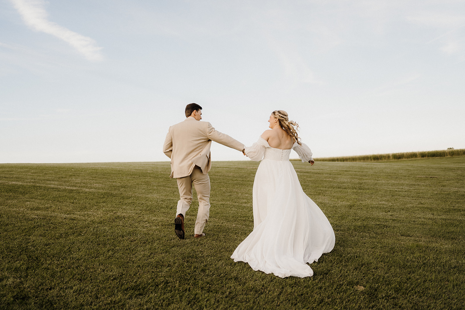 A bride and groom running on the grass holding hands.